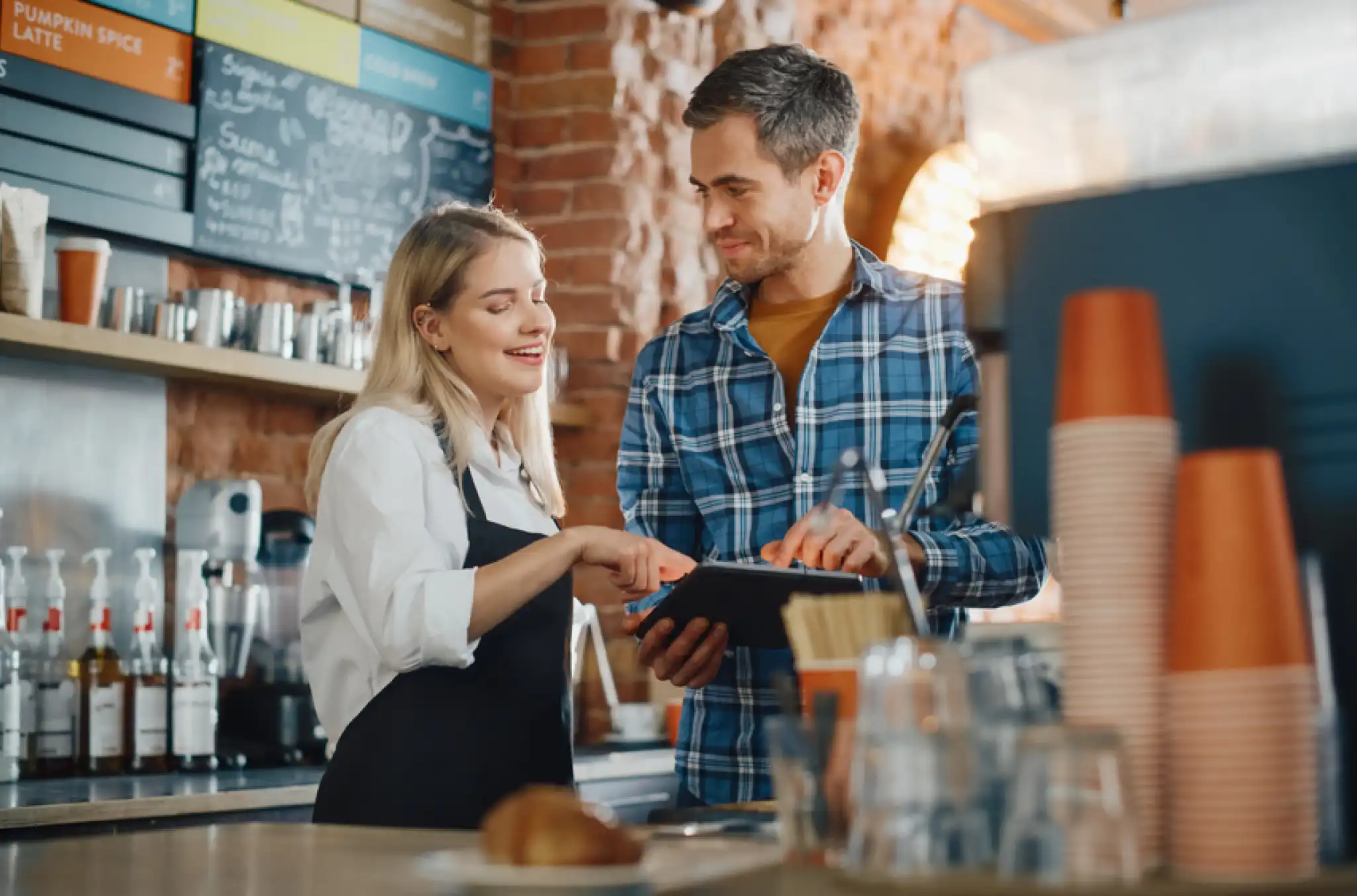 Two employees in a coffee shop overlooking their time tracking software, pleased because they know how to prevent time theft using their software on the tablet in front of them